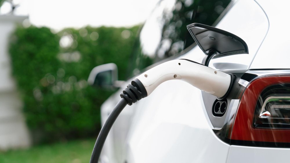 Primer plano del mango del enchufe del cargador EV conectado al puerto del vehículo eléctrico que recarga la batería desde la estación de carga Vehículo EV de diseño moderno y sostenibilidad de energía limpia para un mejor concepto futuro Synchronos